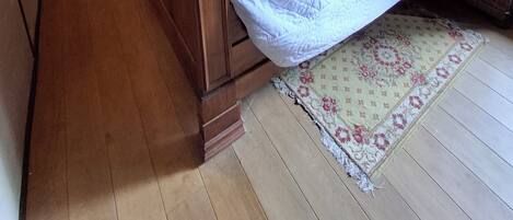 Une chambre à coucher avec un lit en bois, un téléviseur posé sur un meuble en bois, une table de chevet, une chaise, un tapis et un tableau accroché au mur.