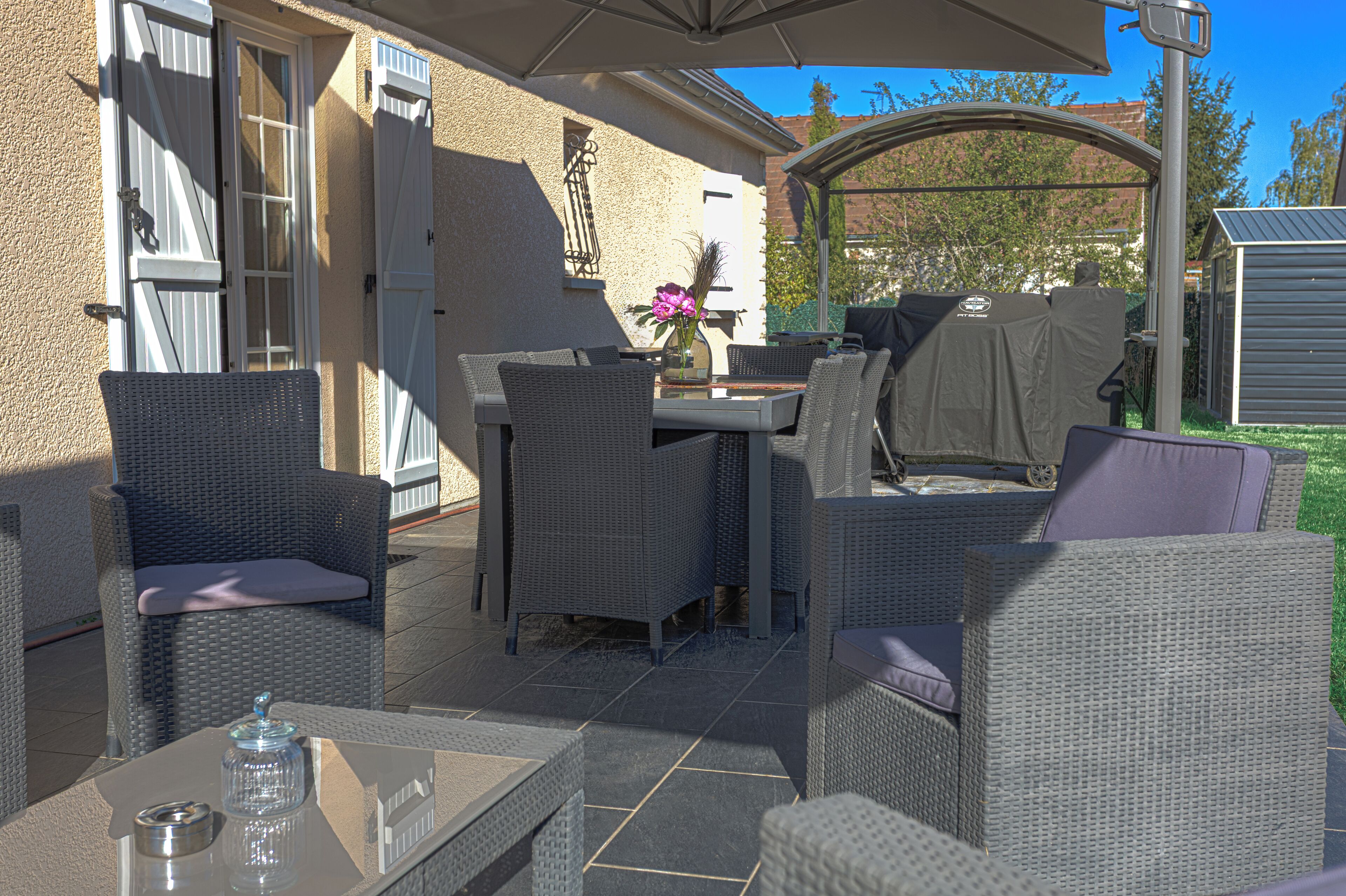 An outdoor patio with wicker furniture, a glass table, and a covered grill area.