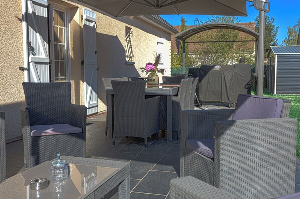 An outdoor patio with wicker furniture, a glass table, and a covered grill area.