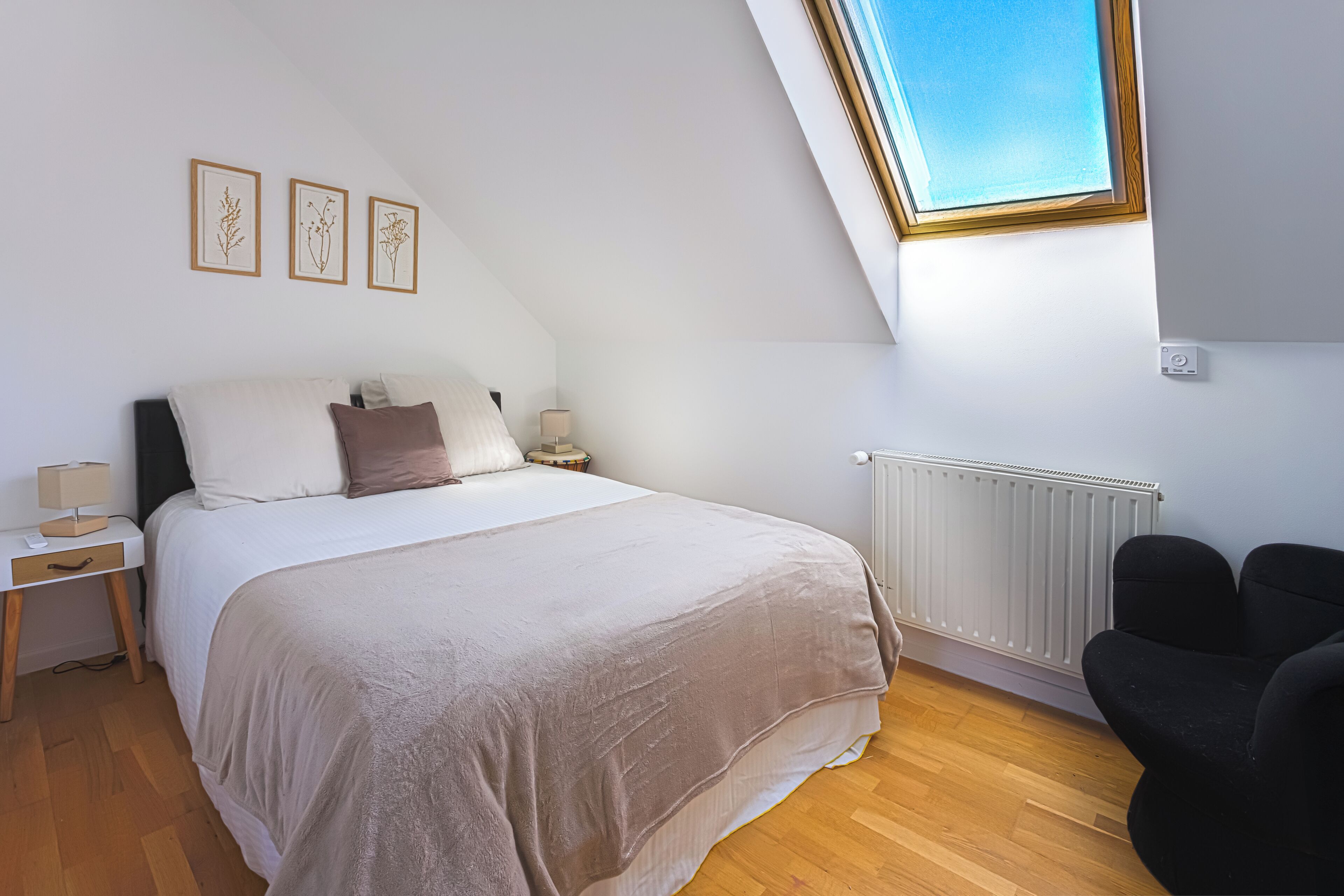 Une chambre à coucher avec un lit, des tables de chevet, une lampe, un radiateur, une fenêtre et une chaise.