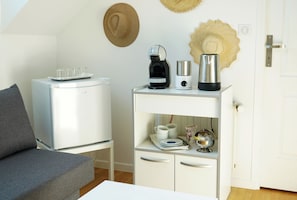 A compact living space with a sofa, a small white cabinet with kitchen appliances, and a door with a handle.