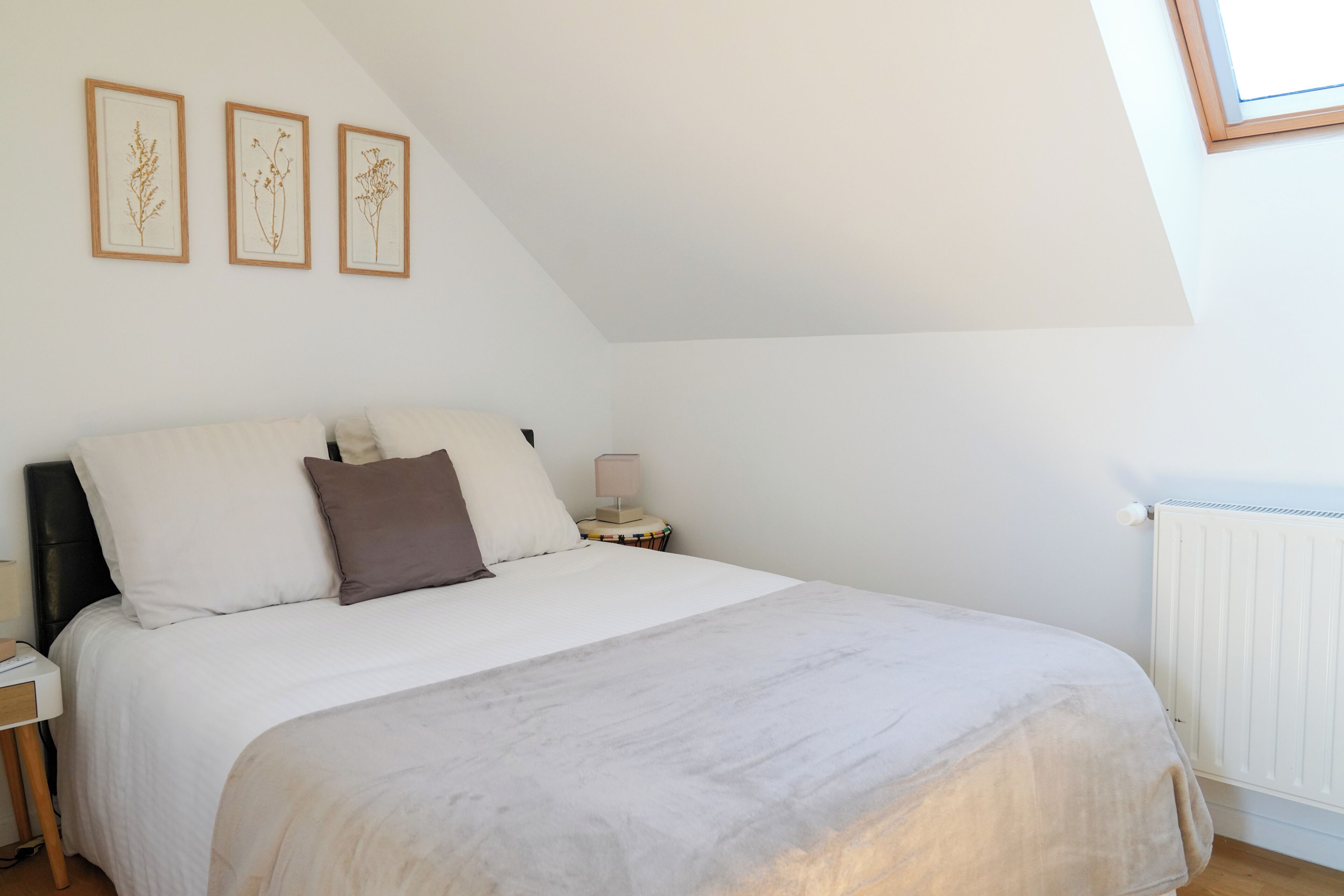 A bedroom with a bed, a nightstand, a lamp, and framed botanical prints on the wall.