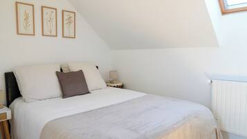 A bedroom with a bed, a nightstand, a lamp, and framed botanical prints on the wall.