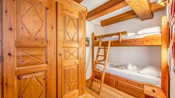Una cama litera de madera con escalera, un armario de madera y un taburete pequeño de madera.