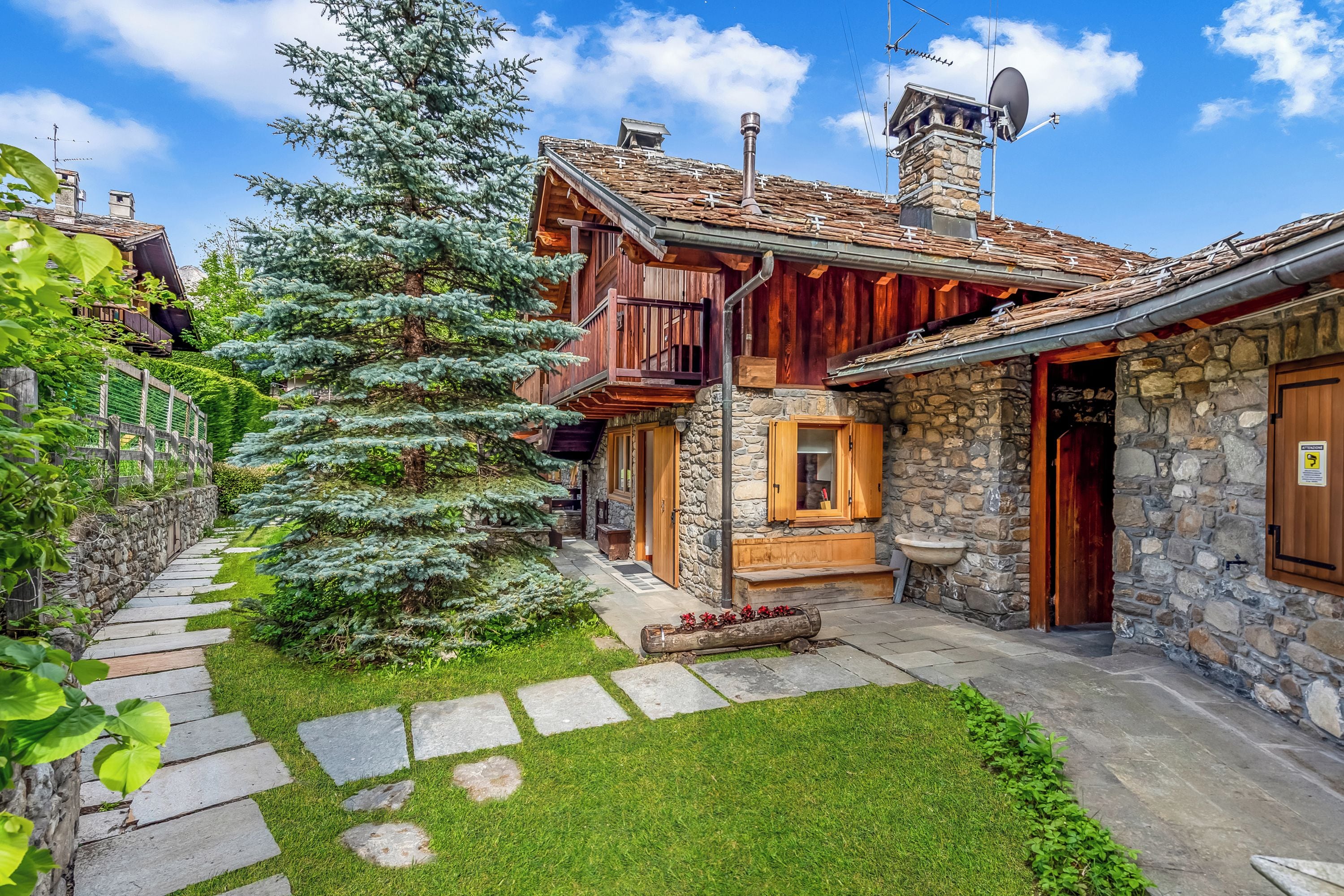 A stone building with a wooden balcony, a stone chimney, and a satellite dish.