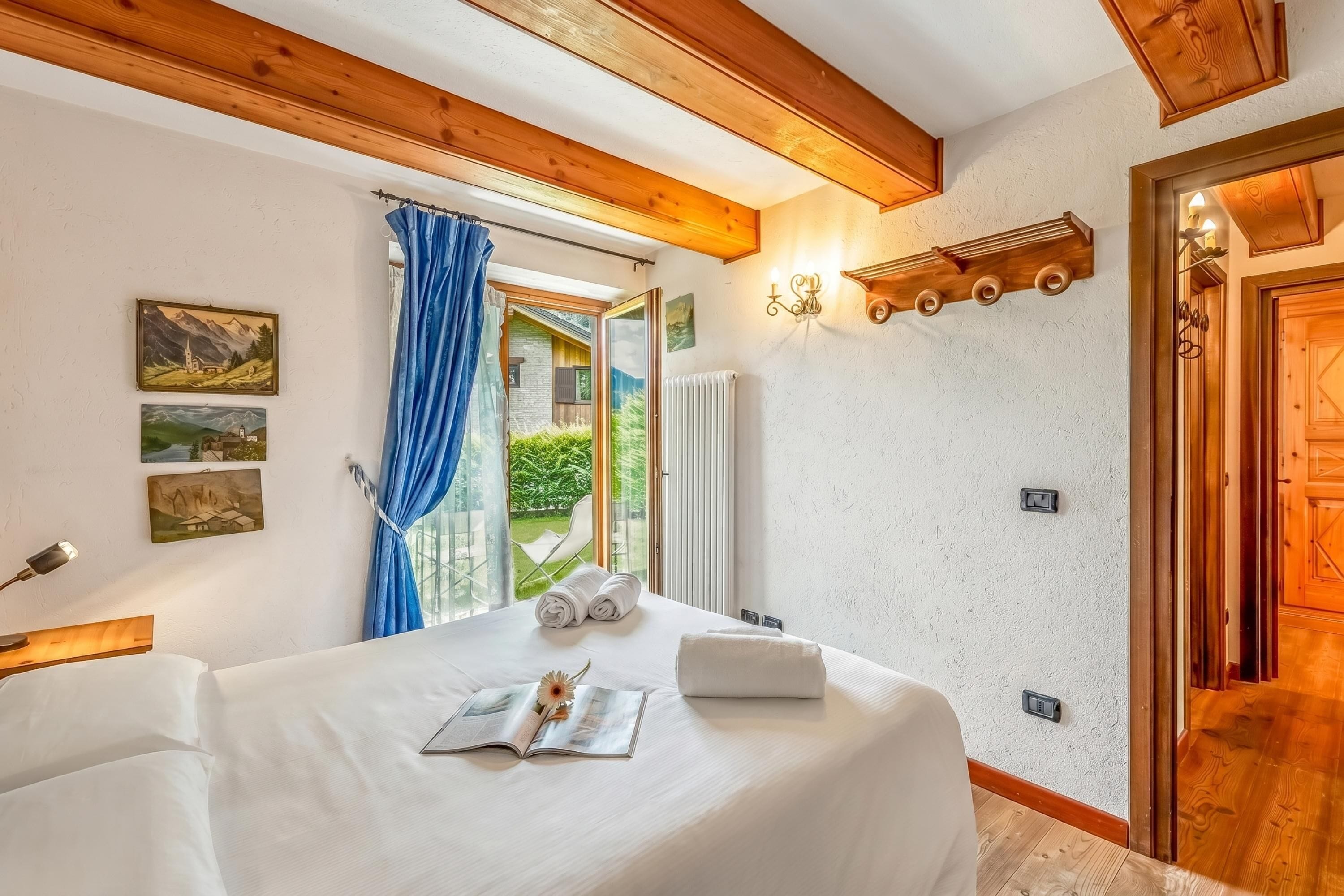 A bedroom with a bed, a window with curtains, a wall-mounted light fixture, and a radiator.