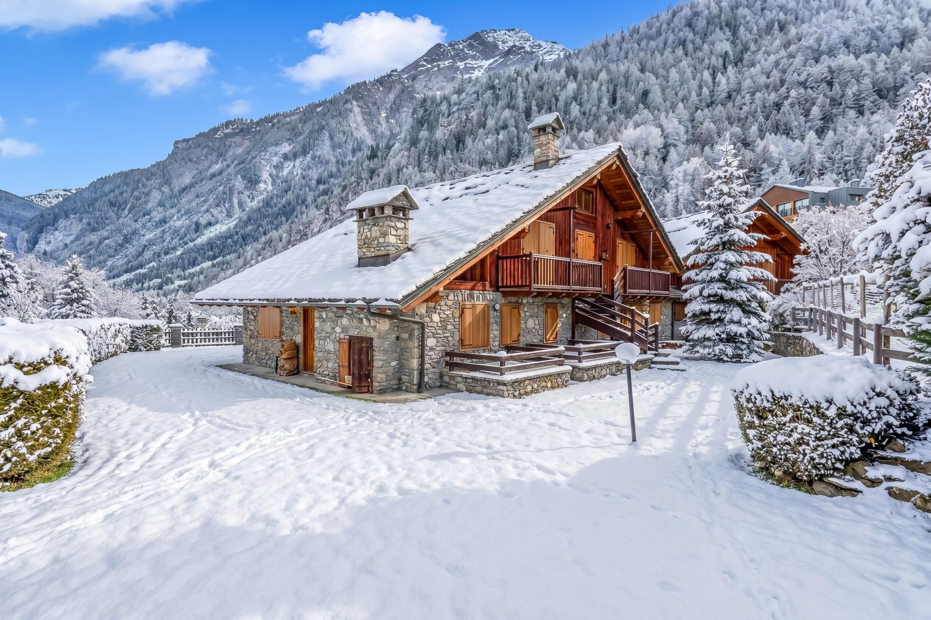 Une cabane en bois, posée sur des fondations en pierre, entourée d’arbres et de montagnes couverts de neige.