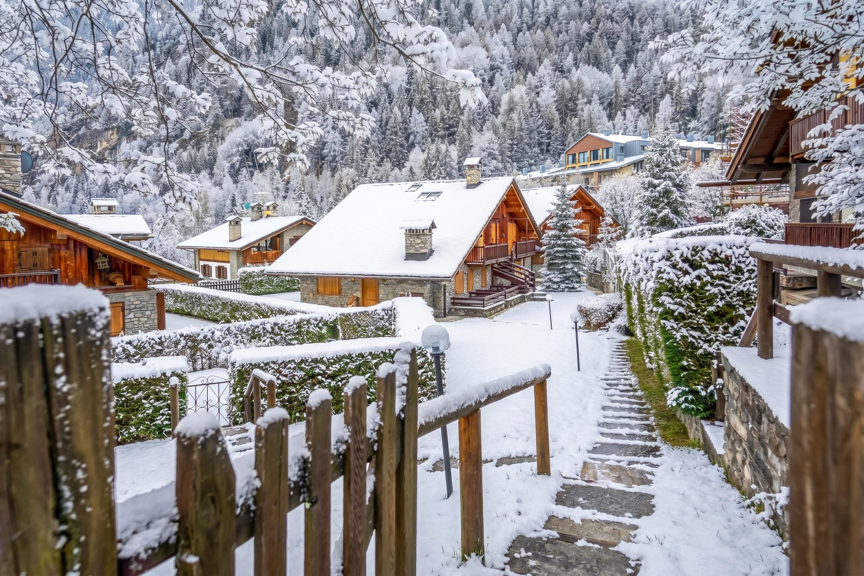 A snow-covered village with wooden buildings, a stone staircase, and a view of the surrounding forest.