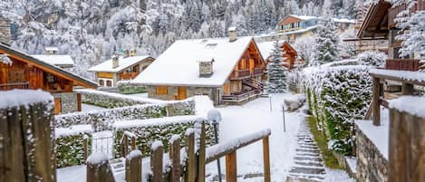 A snow-covered village with wooden buildings, a stone staircase, and a view of the surrounding forest.