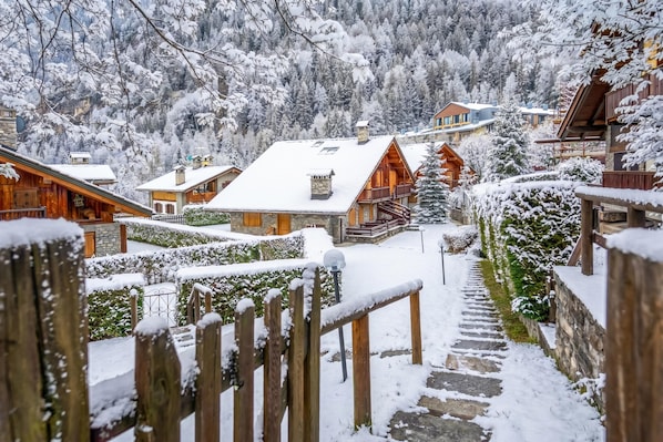 A snow-covered village with wooden buildings, a stone staircase, and a view of the surrounding forest. - Courmayeur Apartment X6 Parking (Courmayeur)