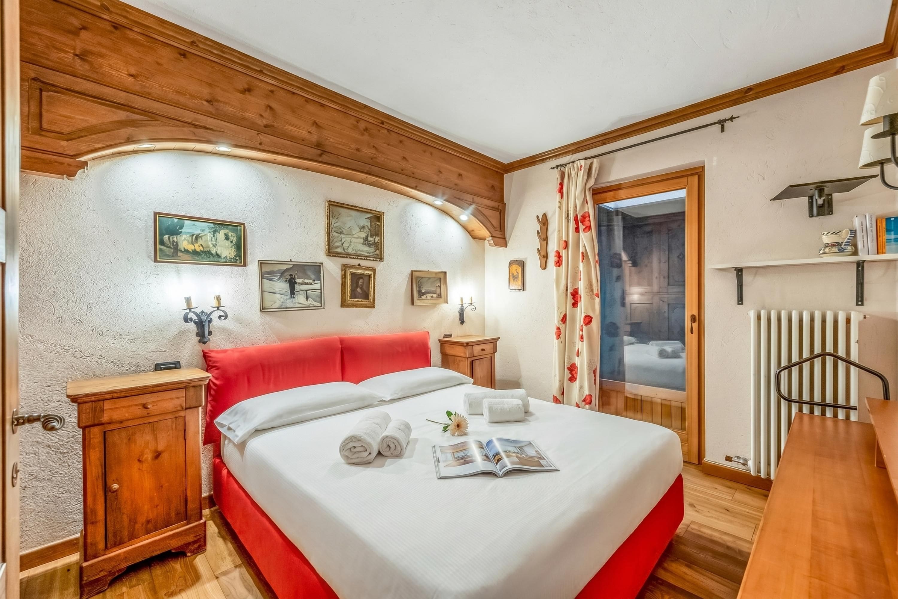 Une chambre comprenant un lit, une tête de lit en bois, des tables de chevet, un radiateur et une porte donnant sur une salle de bain.