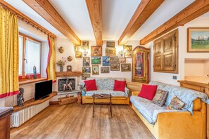 Ein gemütliches Wohnzimmer mit Holzbalken, einem Kamin, einer Sofagarnitur und einer Sammlung gerahmter Bilder an den Wänden.