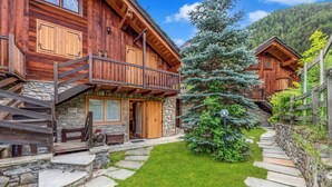 A wooden cabin with a stone staircase, a small lawn, and a large evergreen tree.
