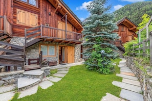 A wooden cabin with a stone staircase, a small lawn, and a large evergreen tree.