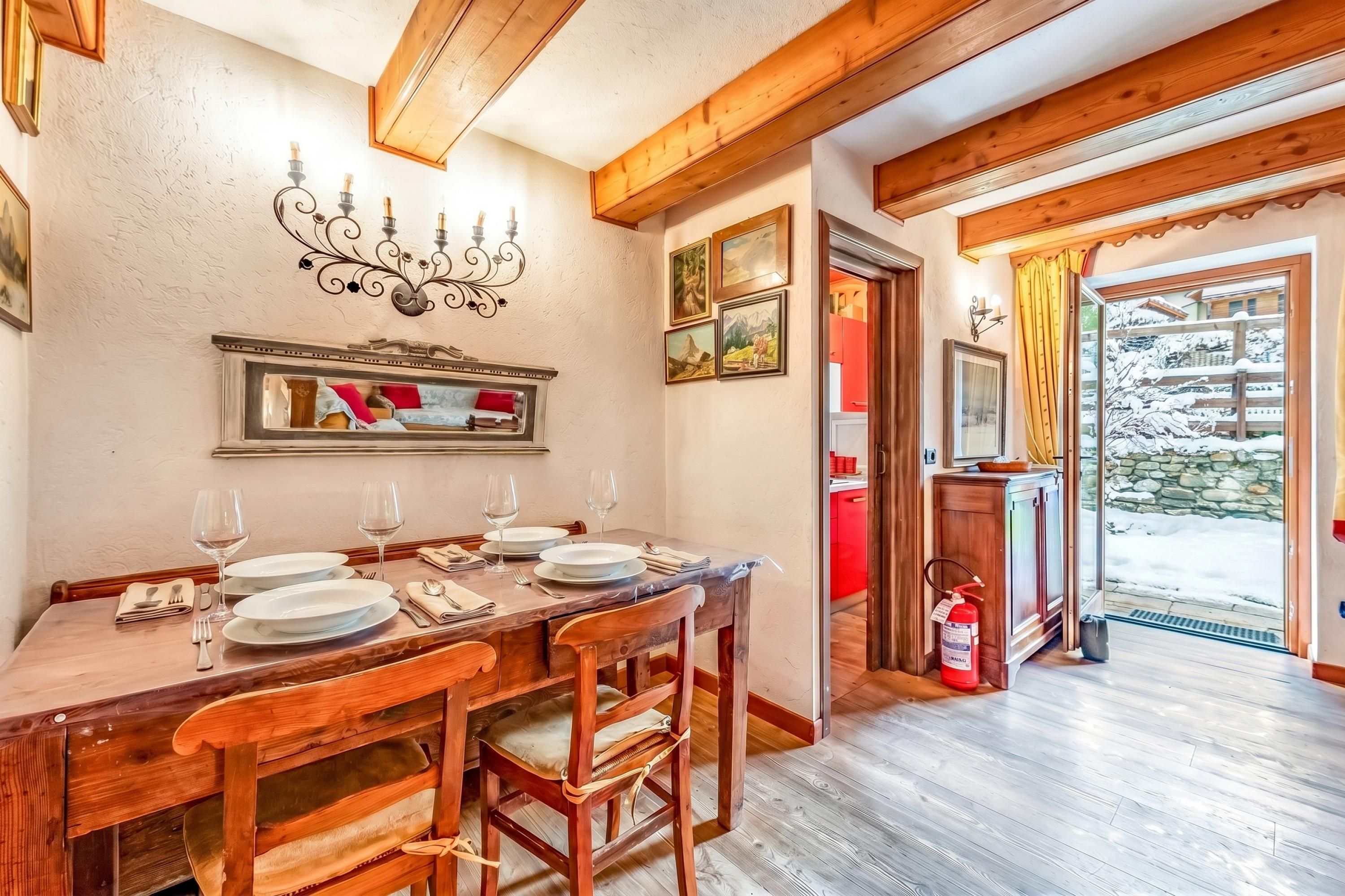 Un comedor con una mesa de madera dispuesta para cuatro personas, sillas, una araña y cuadros en la pared.