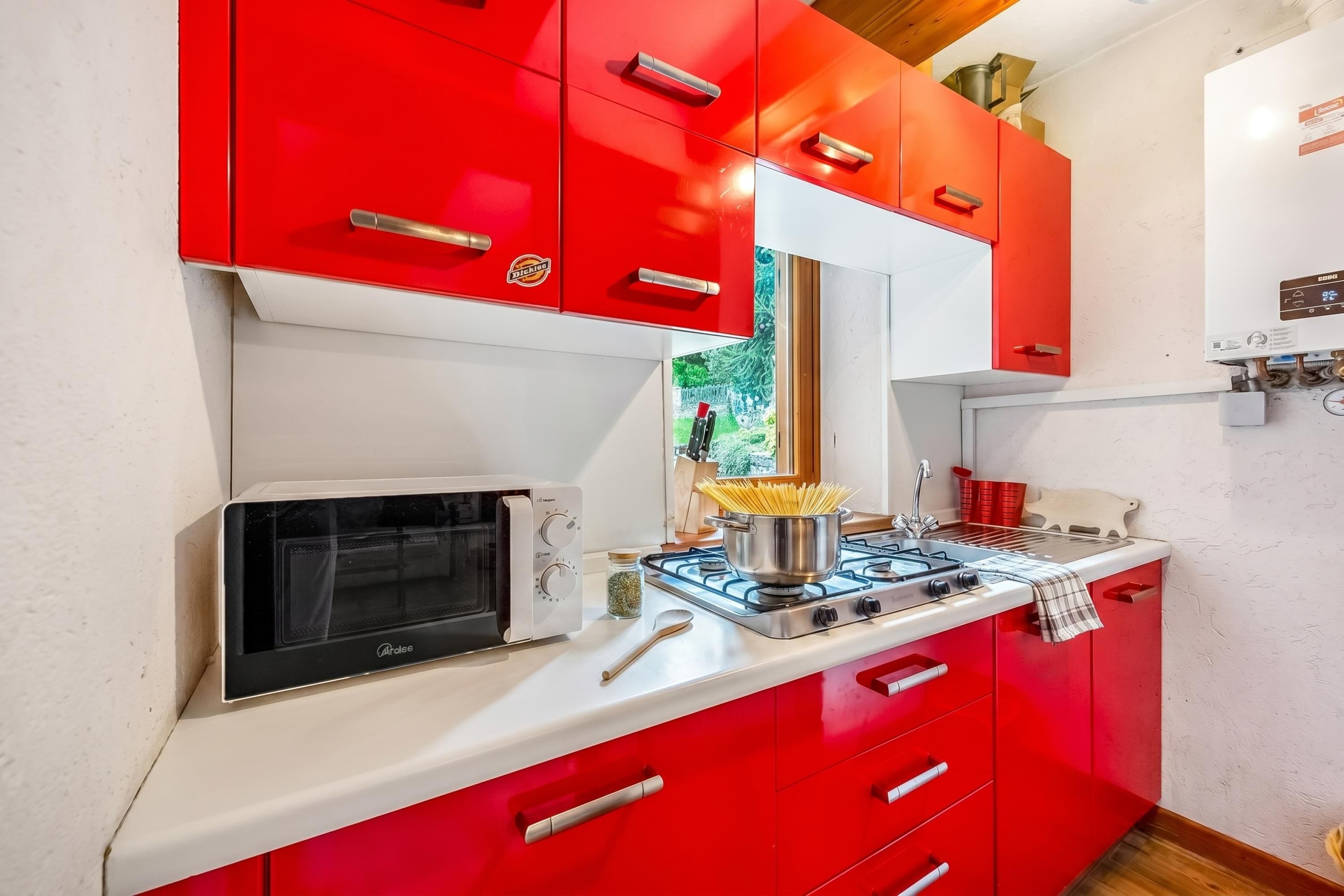 A kitchen with red cabinets, a microwave, a gas stove, and a sink.
