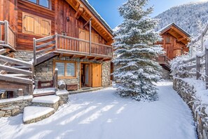 Una cabaña de madera con base de piedra, una escalera de madera y un entorno cubierto de nieve.