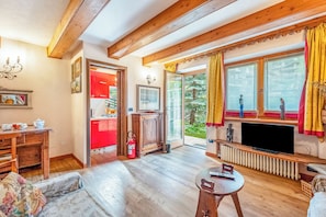 A living room with a sofa, a television, and a fireplace. There is a kitchen visible through an open door.