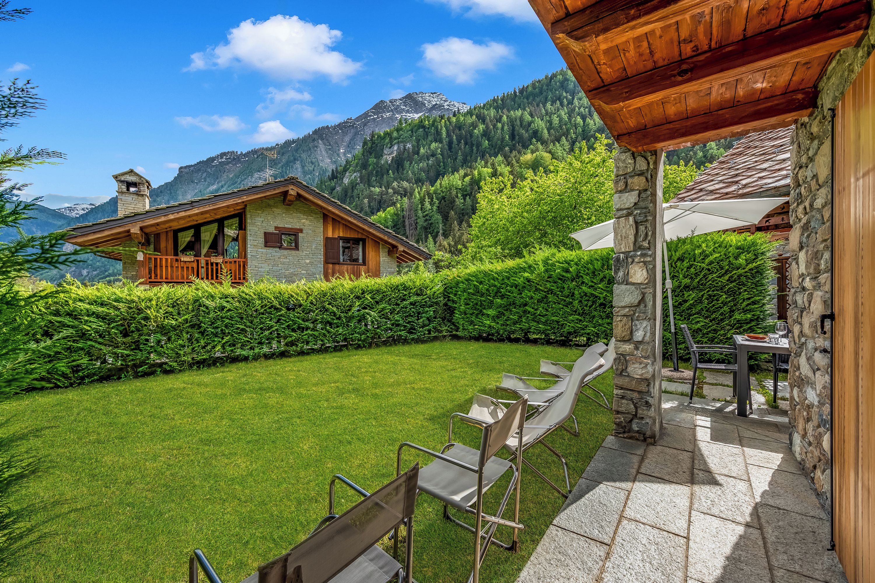 A wooden cabin with stone walls, a grassy backyard, and a mountain view.