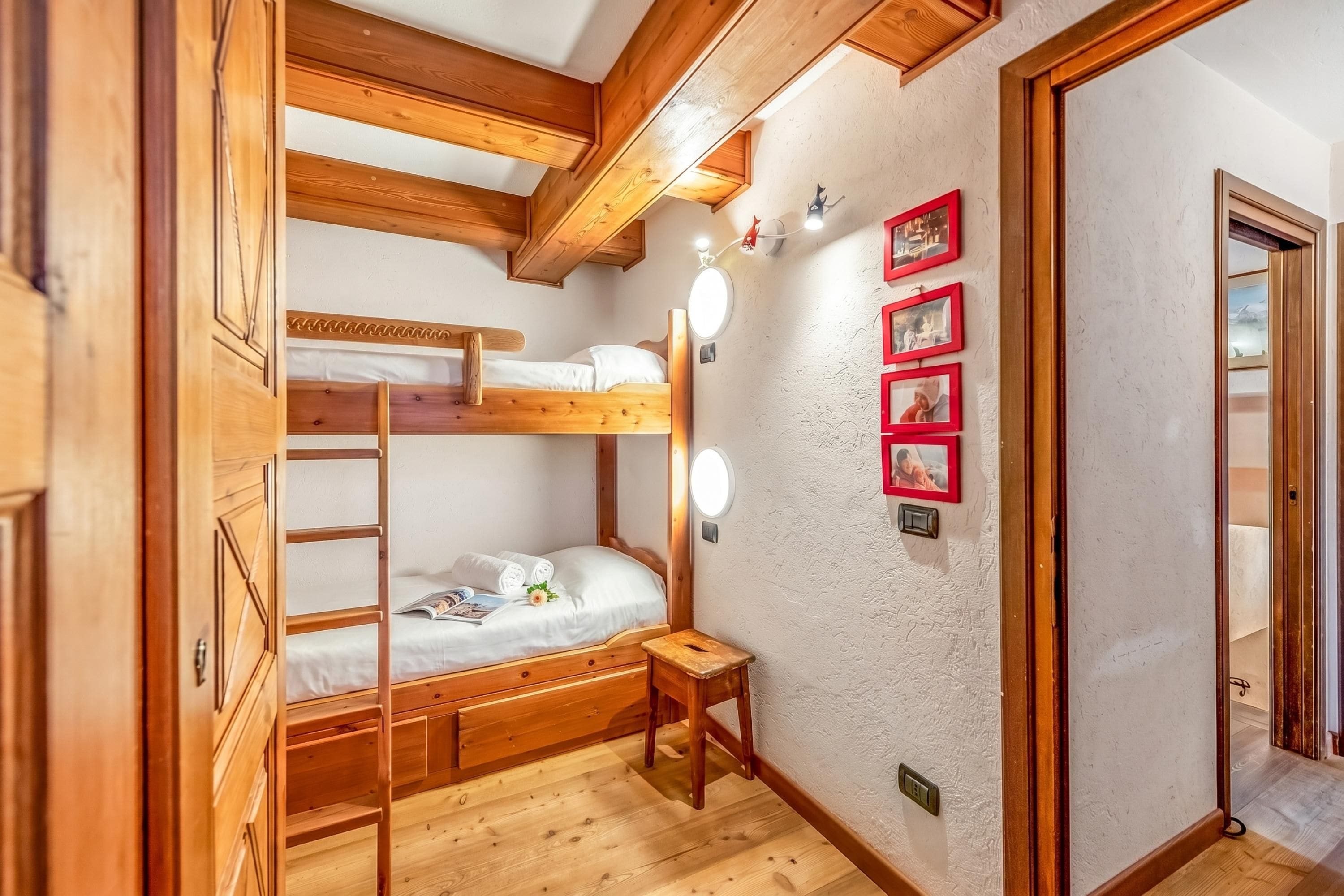A wooden bunk bed room with a small stool, a mirror, and framed pictures on the wall.