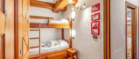 A wooden bunk bed room with a small stool, a mirror, and framed pictures on the wall.