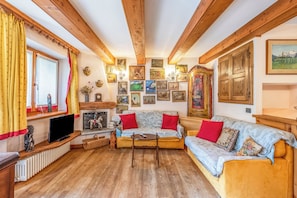 Una sala de estar acogedora con vigas de madera, una chimenea, un conjunto de sofás y una colección de cuadros en las paredes.