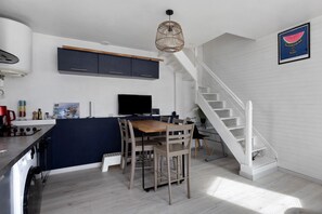 Eine moderne Küche mit einer zentralen Kochinsel, einem Essbereich mit Stühlen, einer Treppe und einem an der Wand montierten Fernseher.