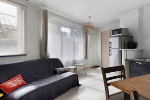 Ein modernes Wohnzimmer mit Sofa, Esstisch und Küchenzeile mit Geräten.
