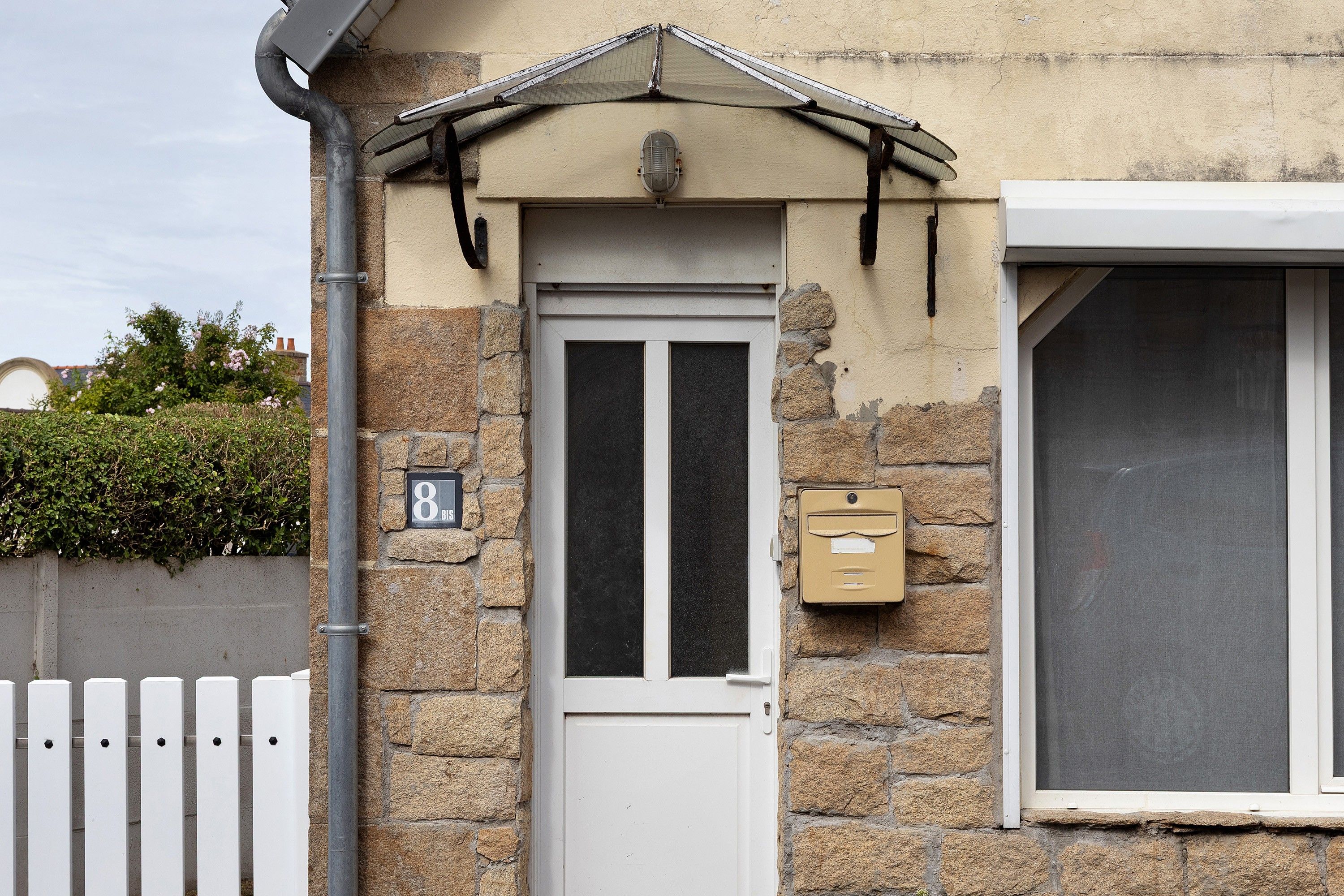A stone building with a white door, a mailbox, and a window with a screen.