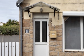 Ein Steinhaus mit einer weißen Tür, einem Briefkasten und einem Fenster mit einem Insektenschutzgitter.