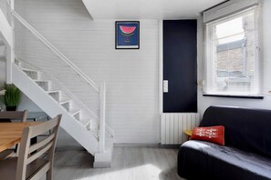 Ein modernes Wohnzimmer mit Treppe, Essbereich und großem Fenster mit Jalousien.