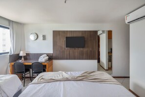 A hotel room with a bed, two chairs, a desk, a TV, a clock, and an air conditioner. - Plaza Suite Ocean View Natal (Natal)