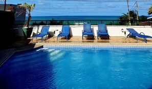 A swimming pool with blue chairs and a view of the ocean.