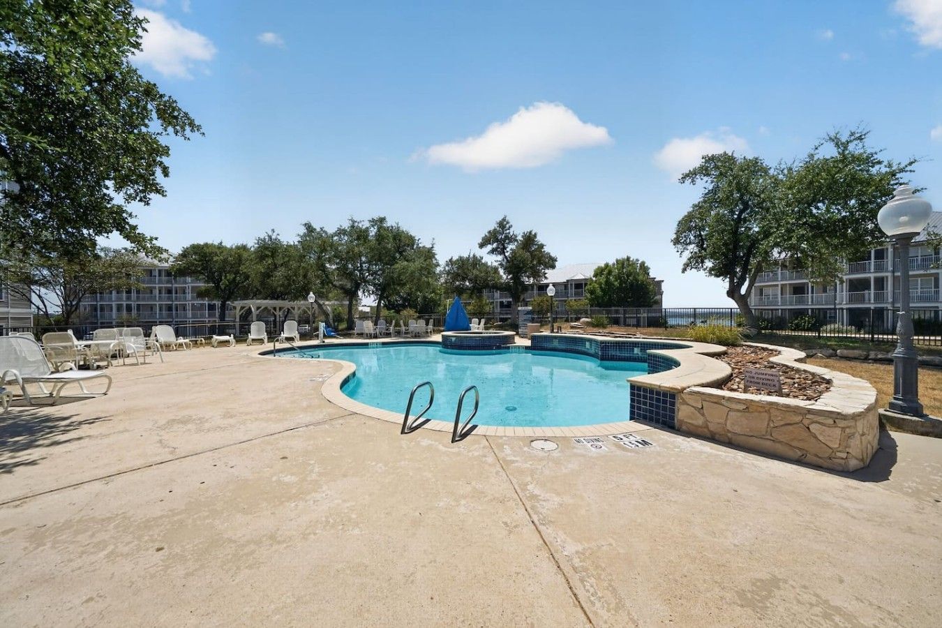 A swimming pool with lounge chairs and a stone deck, surrounded by trees and a building.