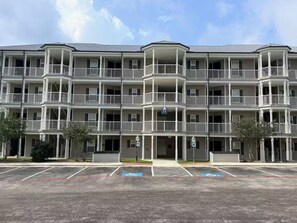 Monikerroksinen hotelli, jossa on parvekkeet, parkkipaikka ja kirkas taivas.