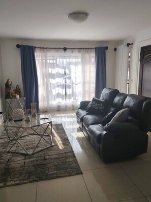 A living room with a black leather sofa, a glass coffee table, and a decorative sculpture on a stand. - Apartment in Heredia, Costa Rica (San Francisco)