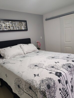A bed with a floral-patterned duvet, a wall-mounted abstract art piece, and a white door. - Apartment in Heredia, Costa Rica (San Francisco)