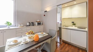 A compact kitchen with a dining area, a microwave, a kettle, and a small window with a plant. - PALERMO, 14 – Garibaldi/Brera Modern Suite (Milan)