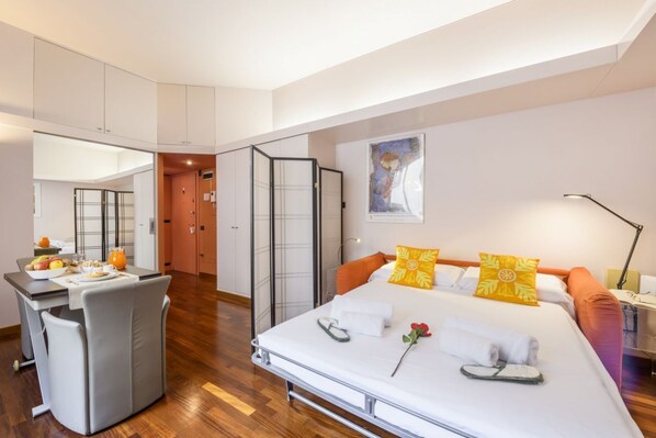 Ein modernes Hotelzimmer mit Bett, Nachttisch und einer kleinen Küchenzeile.