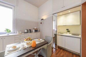 A compact kitchen with a dining area, a microwave, a kettle, and a small window with a plant. - PALERMO, 14 – Garibaldi/Brera Modern Suite (Milan)