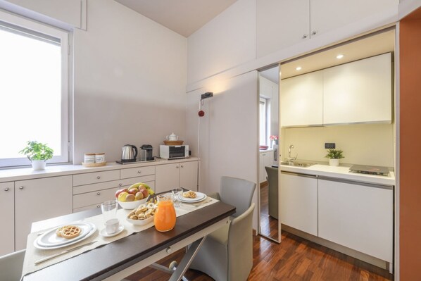 A compact kitchen with a dining area, a microwave, a kettle, and a small window with a plant. - PALERMO, 14 – Garibaldi/Brera Modern Suite (Milan)