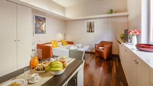 A compact hotel room with a bed, a dining table with breakfast, a sofa, and a small kitchen area. - PALERMO, 14 – Garibaldi/Brera Modern Suite (Milan)