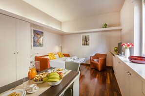 Ein kompaktes Hotelzimmer mit Bett, Frühstückstisch, einer Sitzecke und einer kleinen Küchenzeile.
