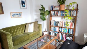 Een woonkamer met een groene bank, een zwarte bank, een glazen salontafel en een boekenplank vol boeken.