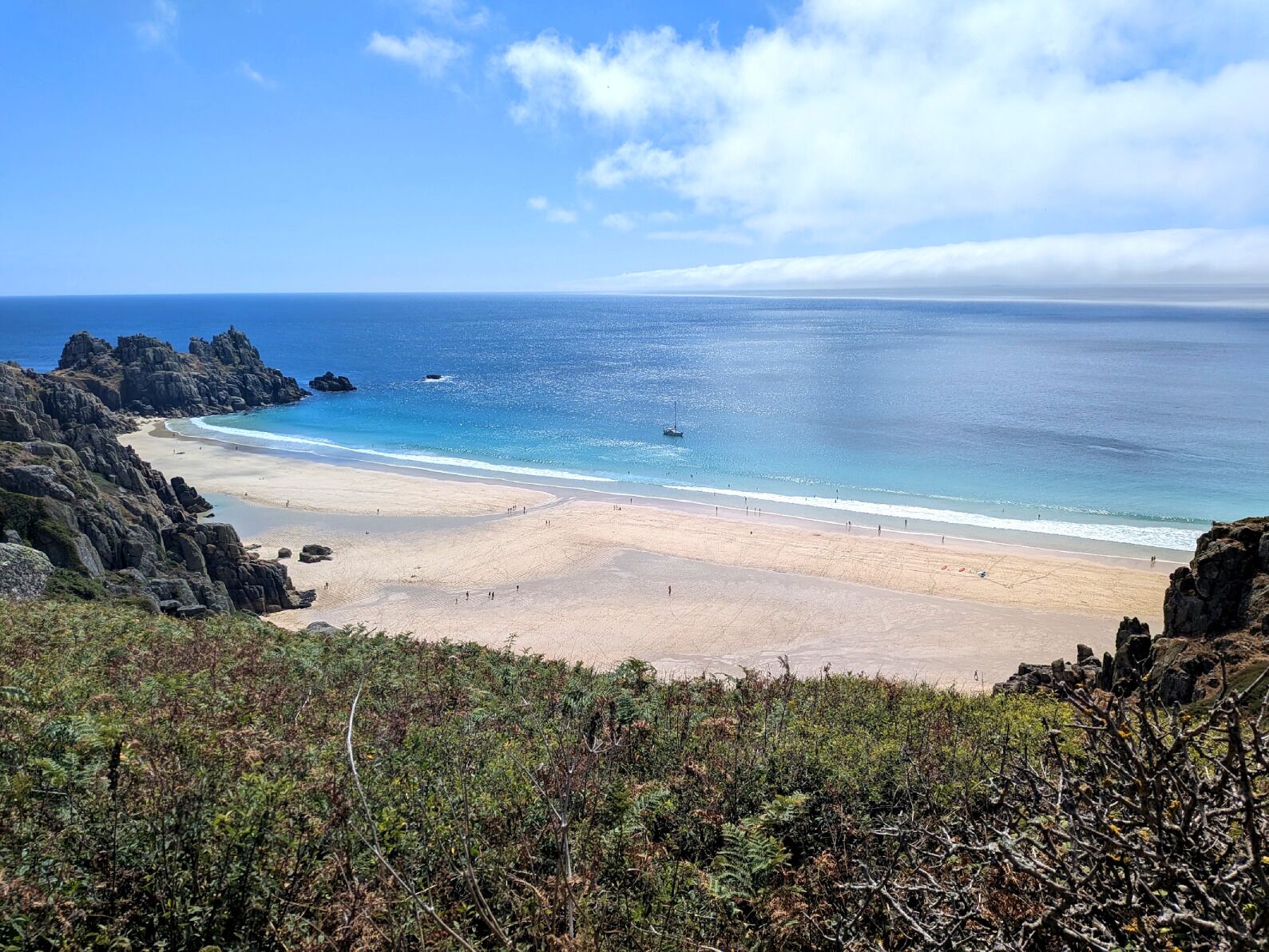 A coastal landscape with a beach, rocky cliffs, and a clear sky.