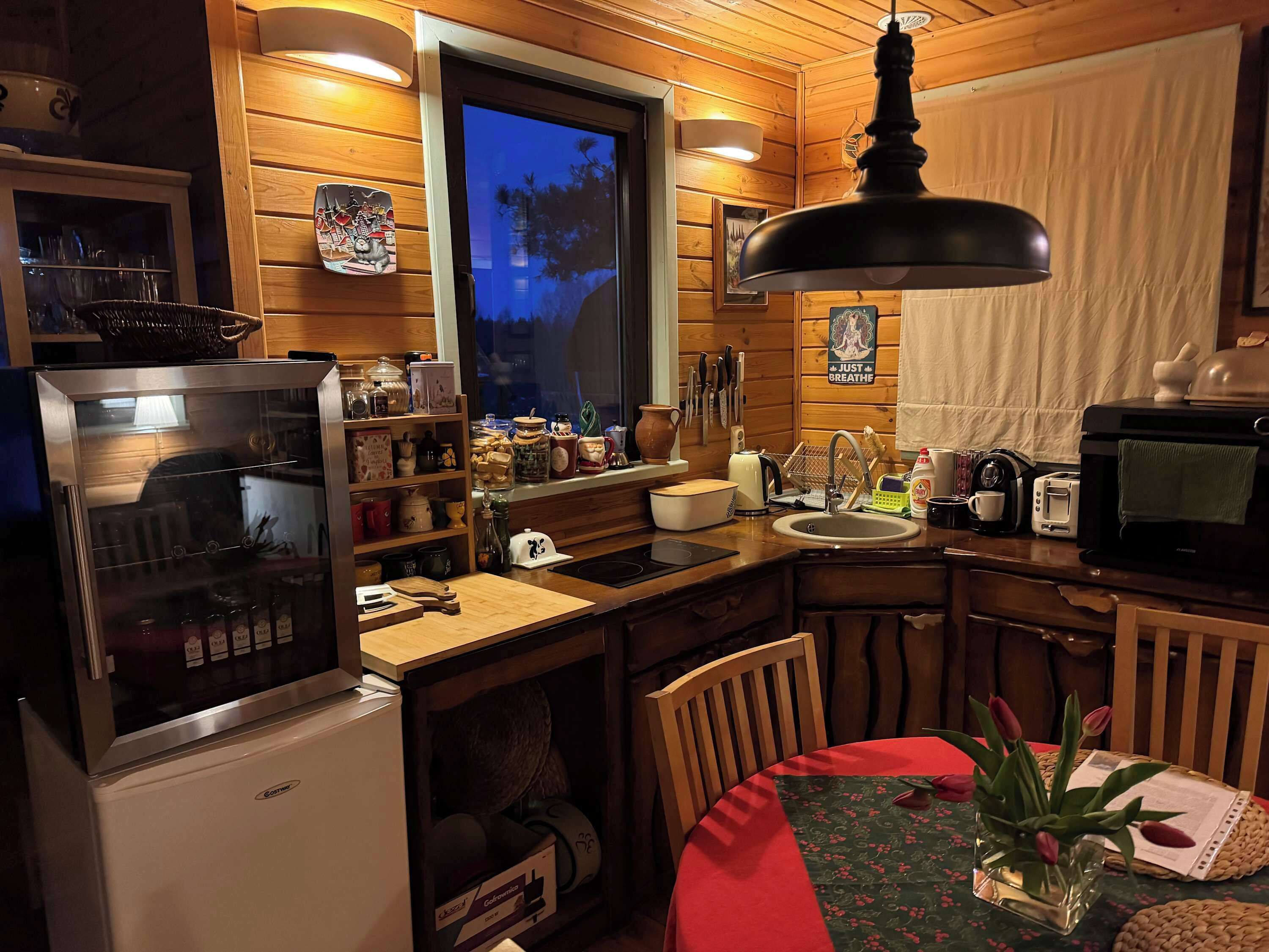 A compact kitchen with wooden walls, a refrigerator, a sink, a microwave, and a dining area with a table and chairs.
