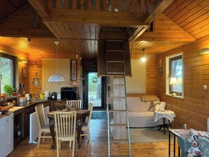 A cozy cabin interior with a dining area, kitchen, and a loft bedroom.