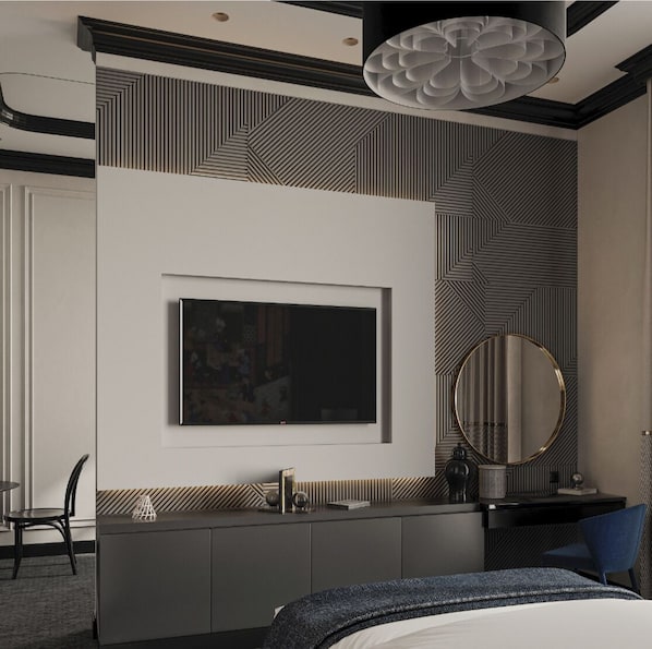 Quarto de hotel moderno com uma televisão de tela plana grande fixada na parede, um espelho redondo, uma escrivaninha com luminária e uma cama com colcha estampada em azul e branco.