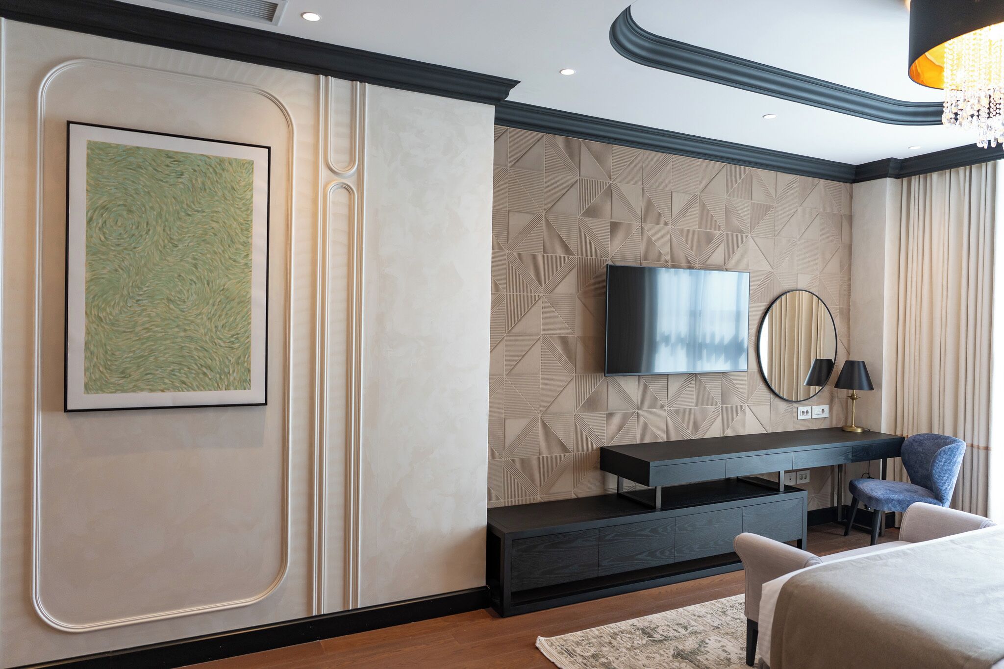 A modern hotel room with a large bed, a desk with a chair, a flat-screen TV mounted on the wall, and a decorative painting.