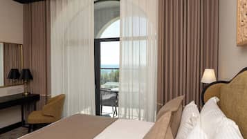 Habitación de hotel con cama, escritorio con lámparas, una silla y vista al exterior a través de un ventanal grande.